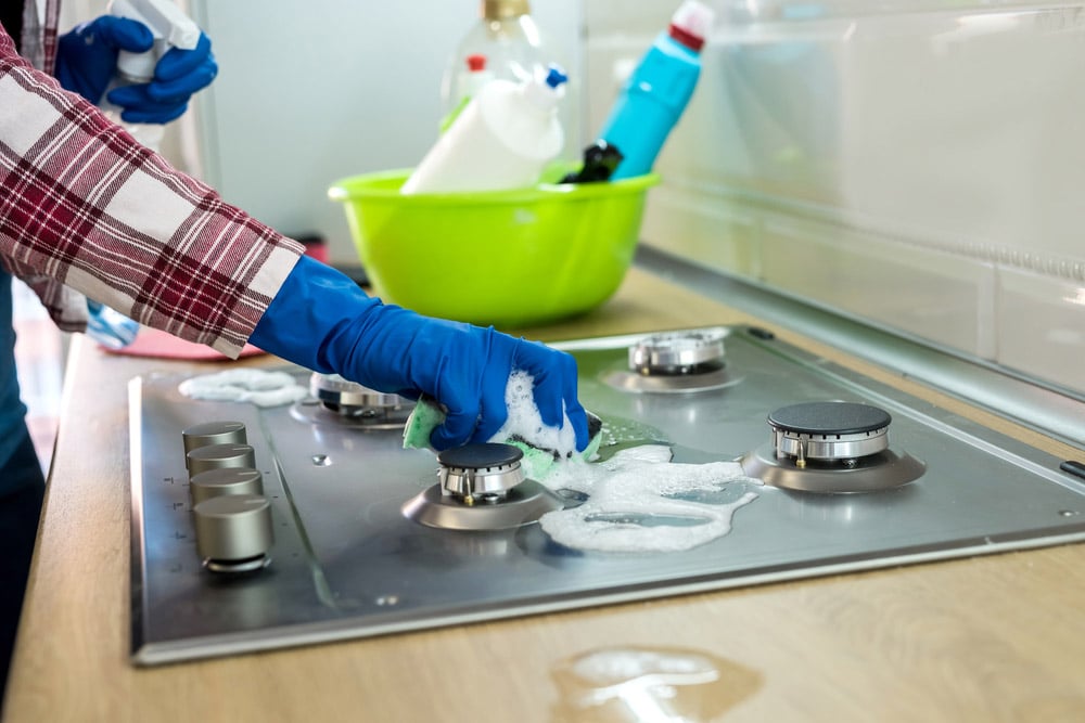 Woman with sponge and rubber protective glove used to wipe down an oven range top