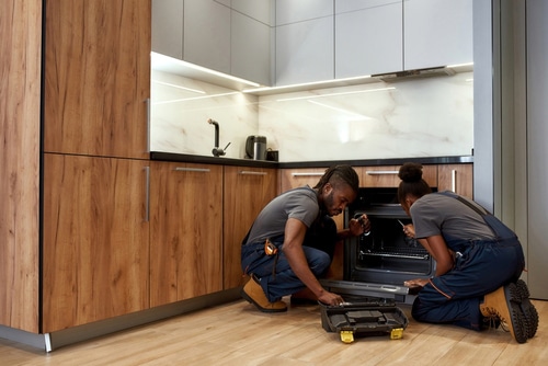 Young African American woman and man repair oven in modern kitchen