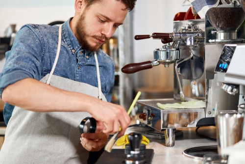 Young bearded man works hard near coffee grinder