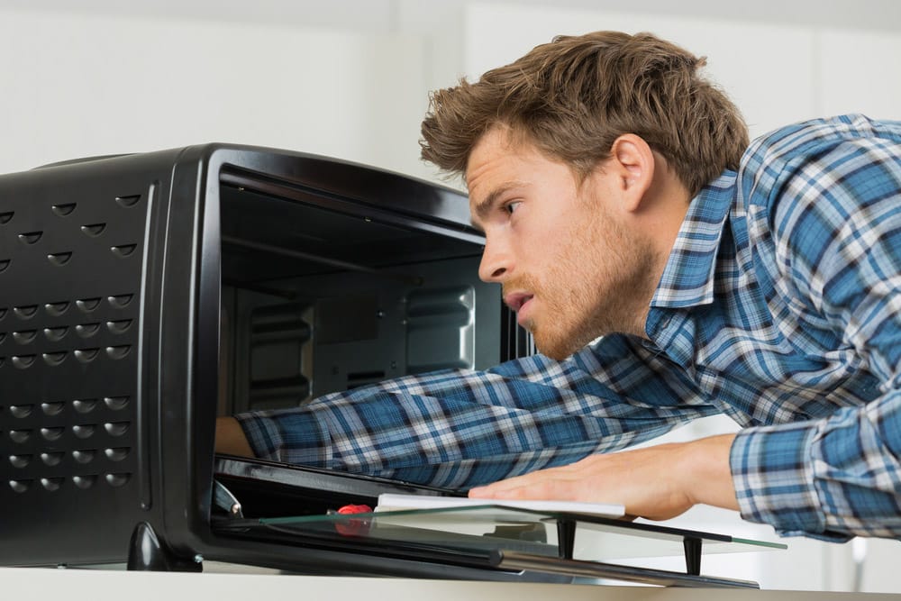 Young male repairman fixing oven in kitchen