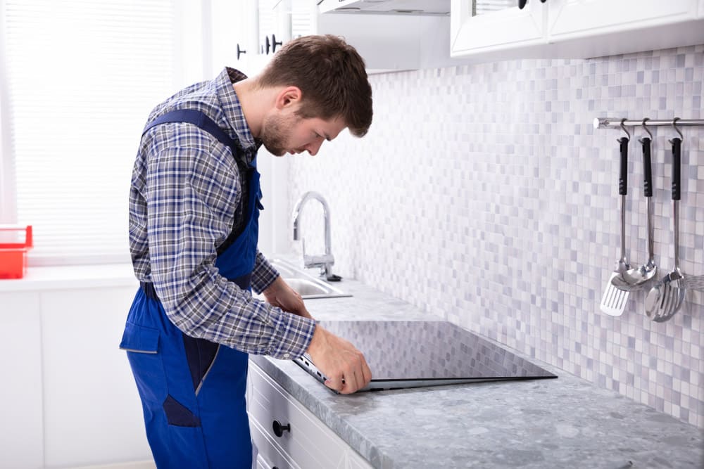 Young Repairman Installing Induction Stove In Kitchen