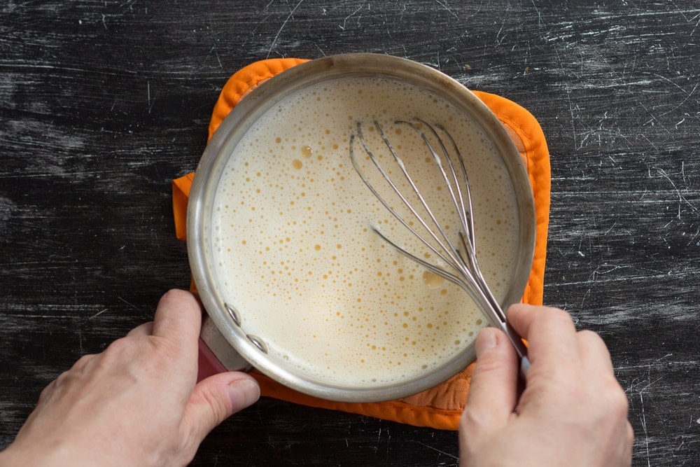 hands stirring hot mix of yolks, starch, sugar and milk to thick making custard cream