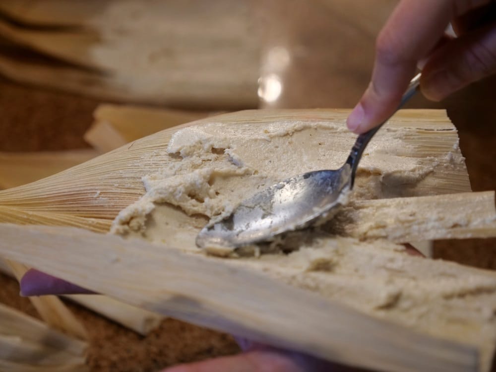 Spreading with the back of a spoon dough (masa) in the husk