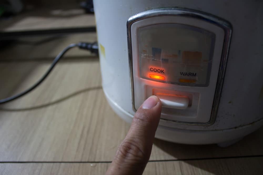 hand pressing rice cooker with orange indicator light