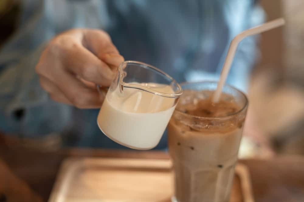 pouring milk cream into iced latte coffee