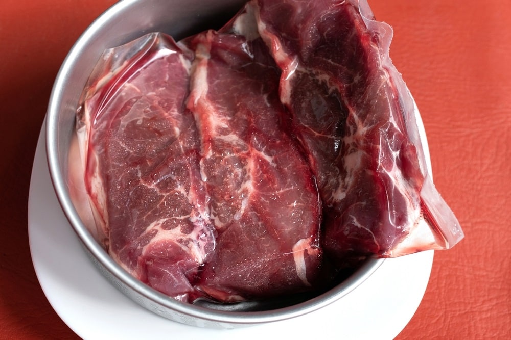 Frozen raw piece of meat in a bowl thawing