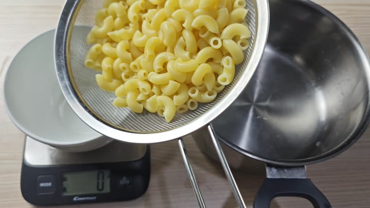 Colander with dry macaroni over scale Colander with dry macaroni over scale